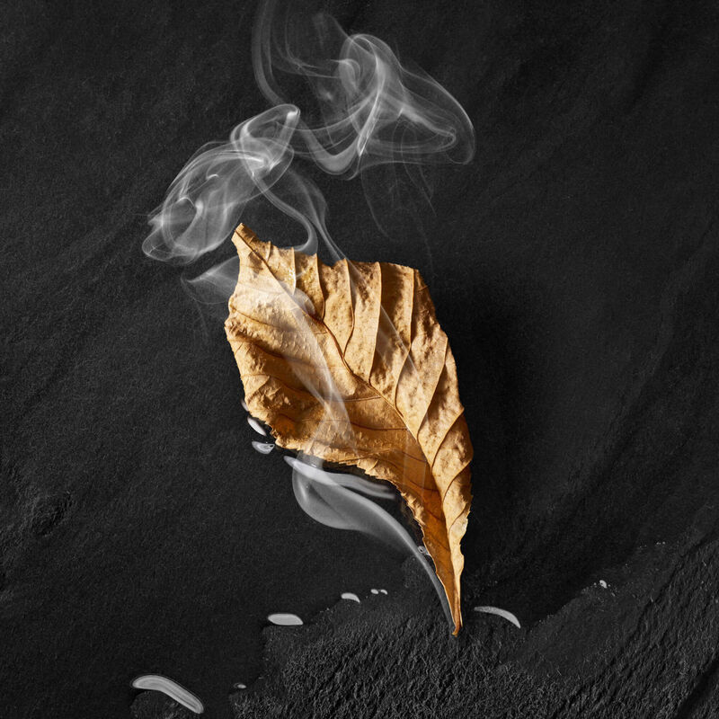 Goudkleurig blad met rook dat er vanaf komt, geplaatst op een donkere ondergrond.