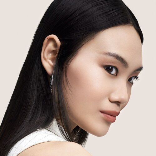 Close-up profile of a young woman with long black hair, wearing subtle makeup and earrings, against a neutral background.