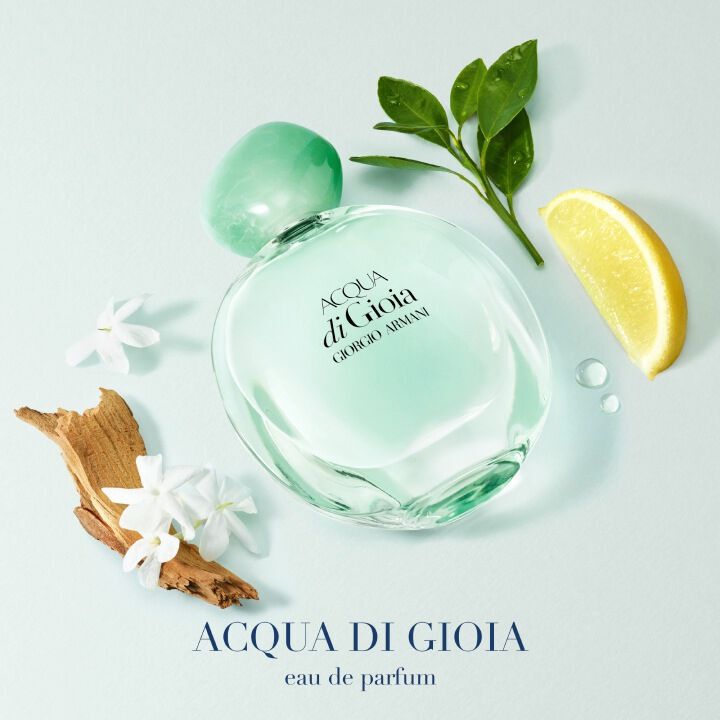 Acqua di Gioia Eau de Parfum bottle with green mandarin, cedarwood, jasmine, and green leaves, styled on a pale blue background.