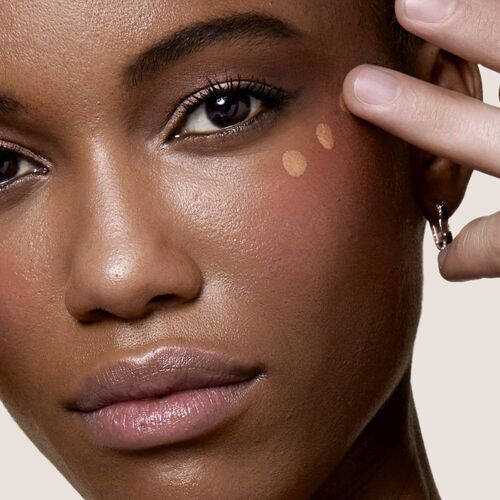 A close-up of a woman applying foundation to her cheek, showcasing her smooth skin and natural makeup look.