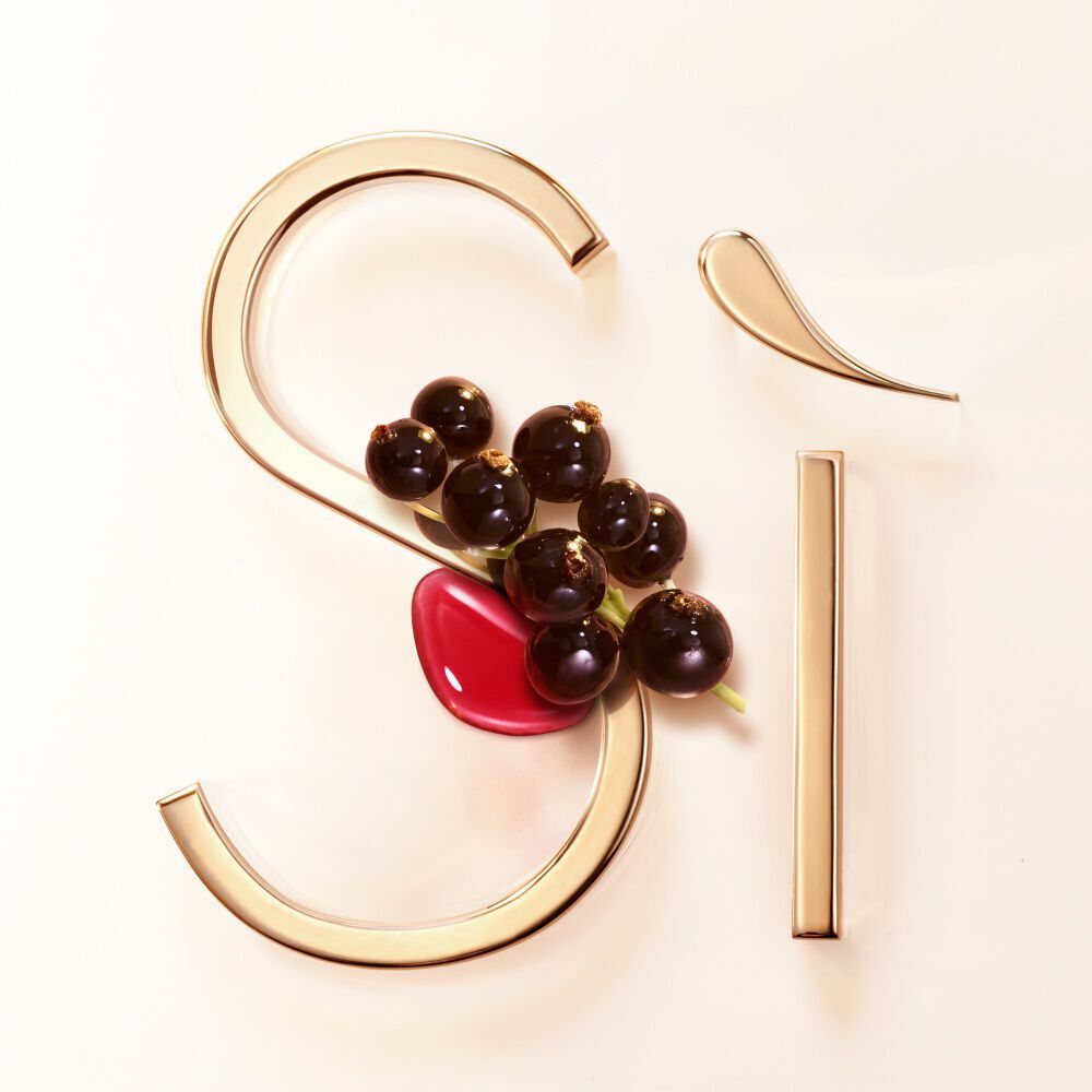 Blackcurrant berries against the gold Si signature on a blush background — blackcurrant nectar top note of Si Eau de Parfum by Giorgio Armani.