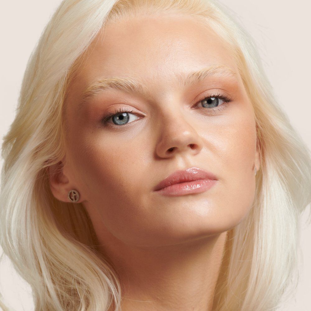 Close-up portrait of a model with long, light blonde hair and natural makeup, gazing slightly to the side.