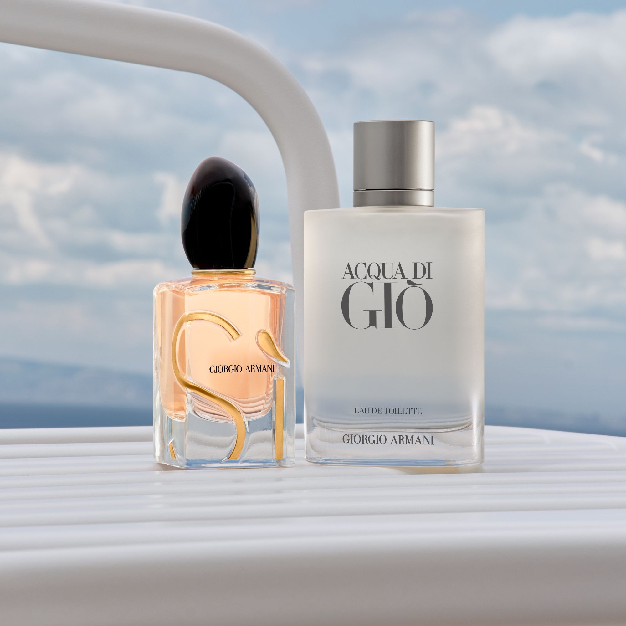 Armani-iconen: de stralende Si en frisse Acqua di Gio. Geplaatst op de reling van een wit jacht voor een serene zee en lucht, belichamen ze tijdloze elegantie en de geest van een luxueus uitje aan de kust.​