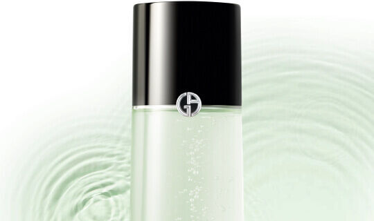 Alt-tekst: Een flesje huidverzorgingsproduct met een zwarte dop en het logo van Giorgio Armani, op een achtergrond met golven van water.