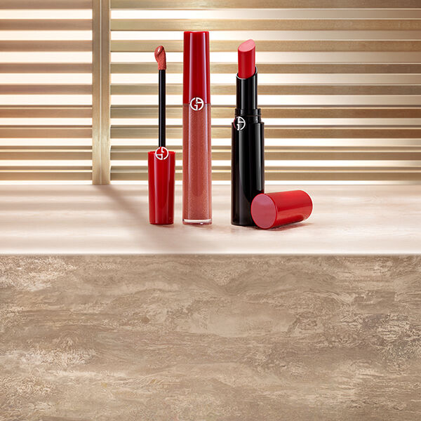 Rode vloeibare lippenstift en rode lippenstift van Giorgio Armani, gepresenteerd op een stenen oppervlak voor zonverlichte jaloezieen.