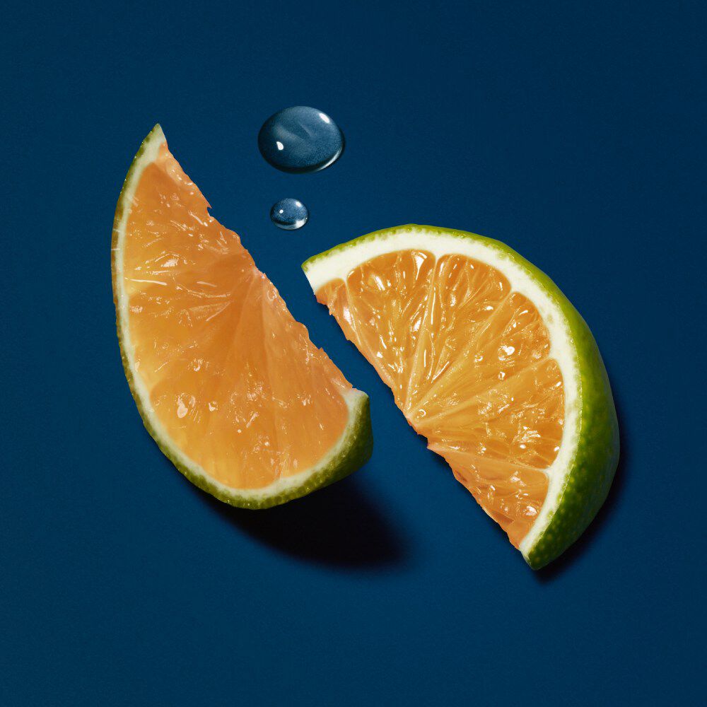 Twee stukken citrusvrucht, een sinaasappel en een limoen, met druppels water op een diepblauwe achtergrond.
