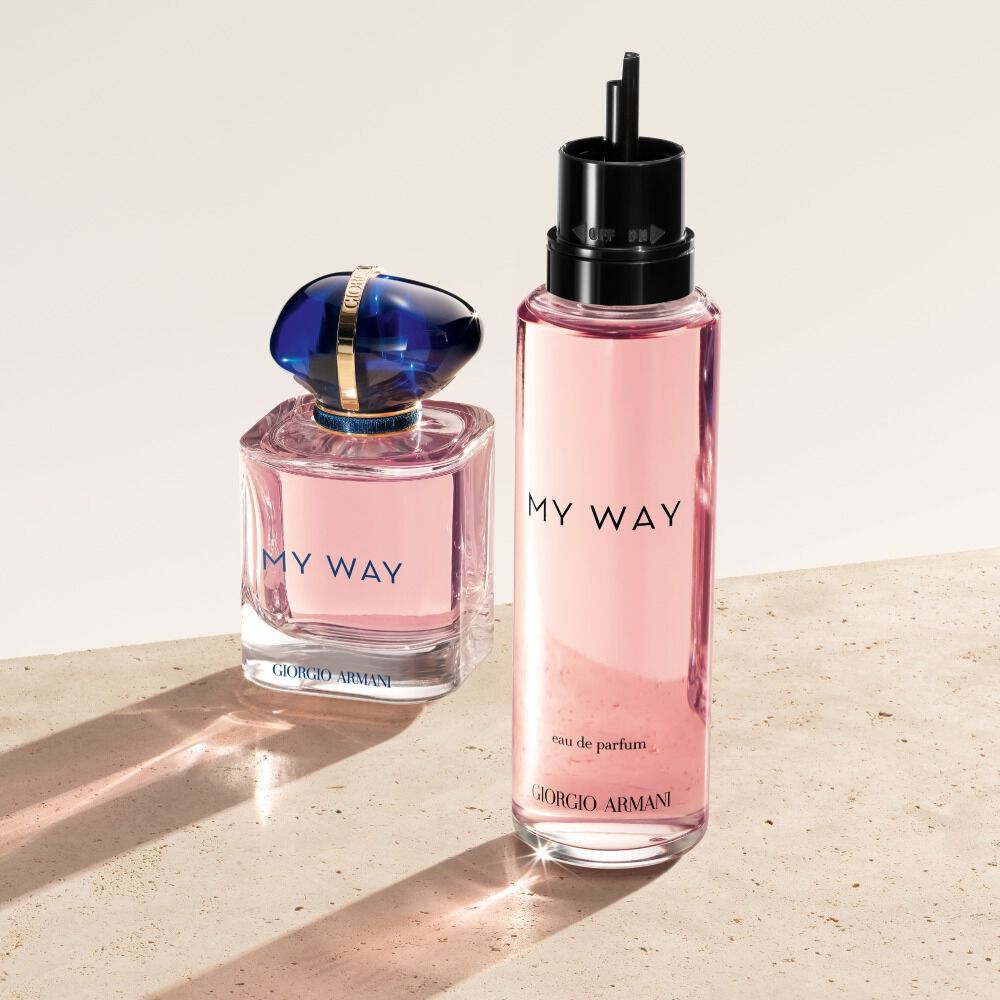 Een flesje en een navulling van Giorgio Armani My Way Eau de Parfum. Het originele flesje, een zacht roze met een blauwe dop, staat naast zijn hogere, doorschijnende roze navul-tegenhanger. Ze rusten op een bleke, getextureerde ondergrond.