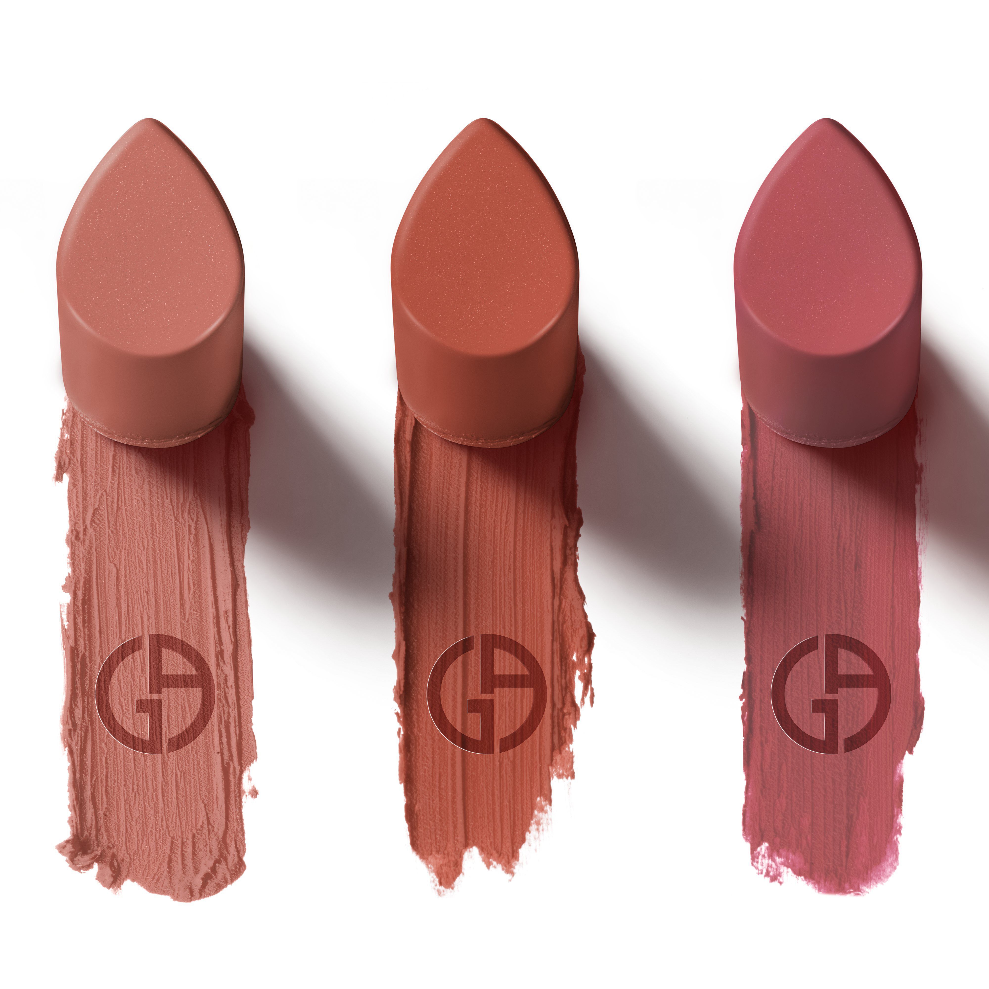 Three lip products with pointed caps are displayed above swatches of their shades on a white background. The swatches range from light nude to deep rose. Each swatch features the logo of the brand subtly printed within it.