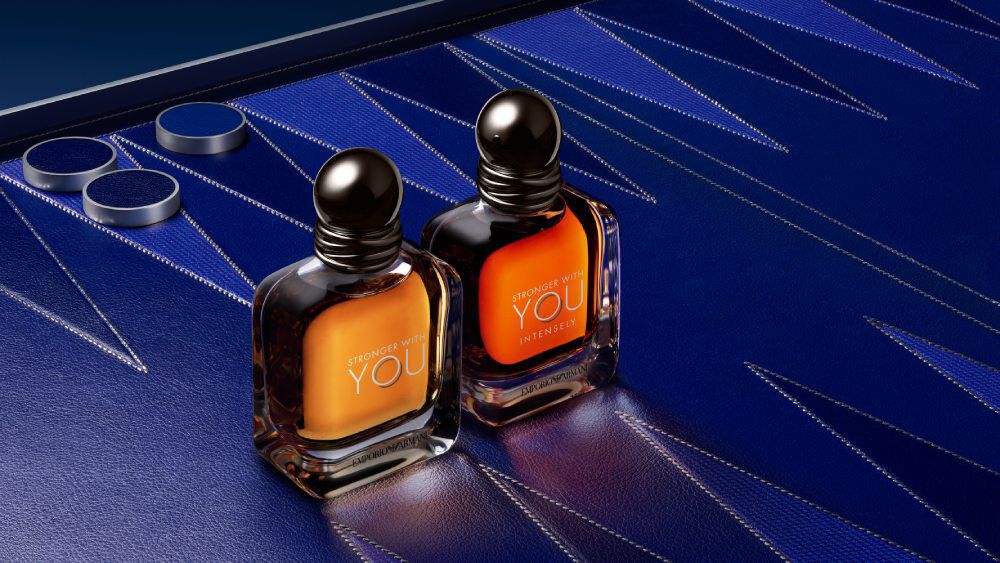 Armani STRONGER WITH YOU EAU DE TOILETTE bottles on a blue geometric background, showcasing the modern, masculine bottle design and vibrant amber hue.