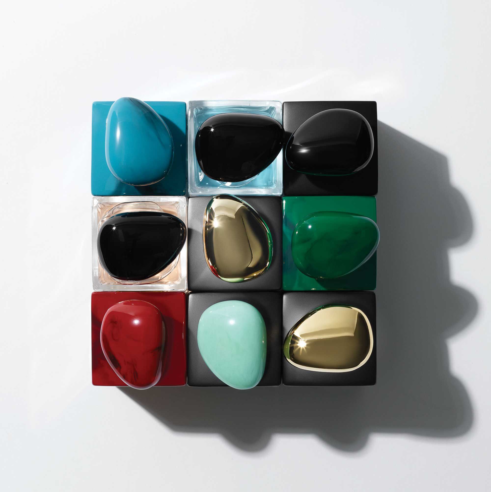 A flat lay of nine glossy, teardrop-shaped objects in various colors, arranged in a 3x3 grid on a light background. Colors include turquoise, black, red, green, and gold.