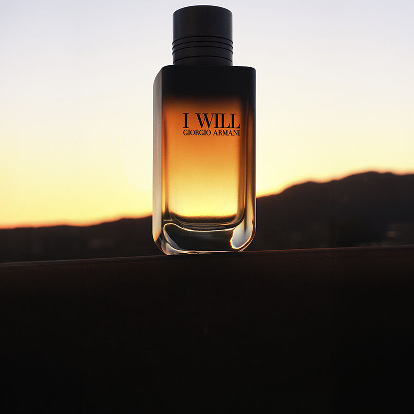 Flacon van de I WILL-geur van Giorgio Armani tegen een landschap bij zonsondergang.