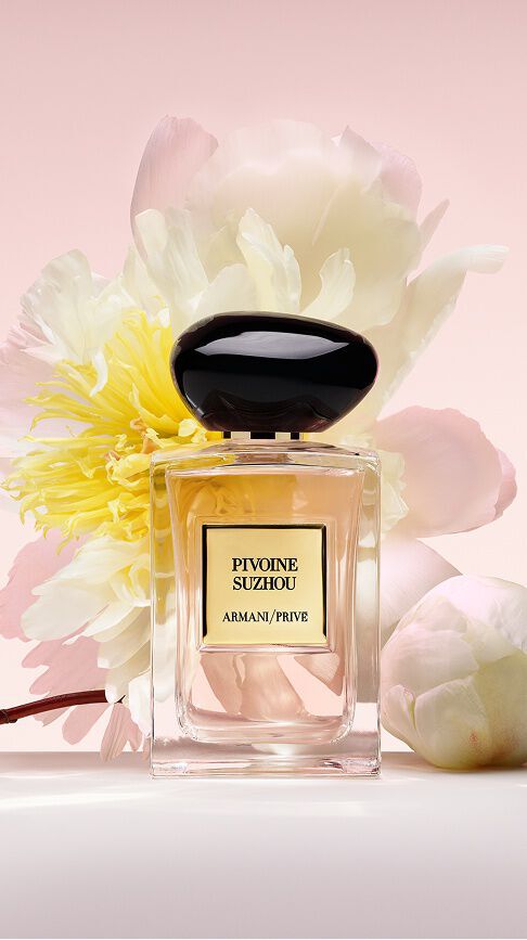 Armani/Prive Pivoine Suzhou: een heldere glazen flacon met een zachtroze geur, genesteld tussen weelderige witte en gele pioenen, die de gratie en stralende schoonheid van de natuur viert.