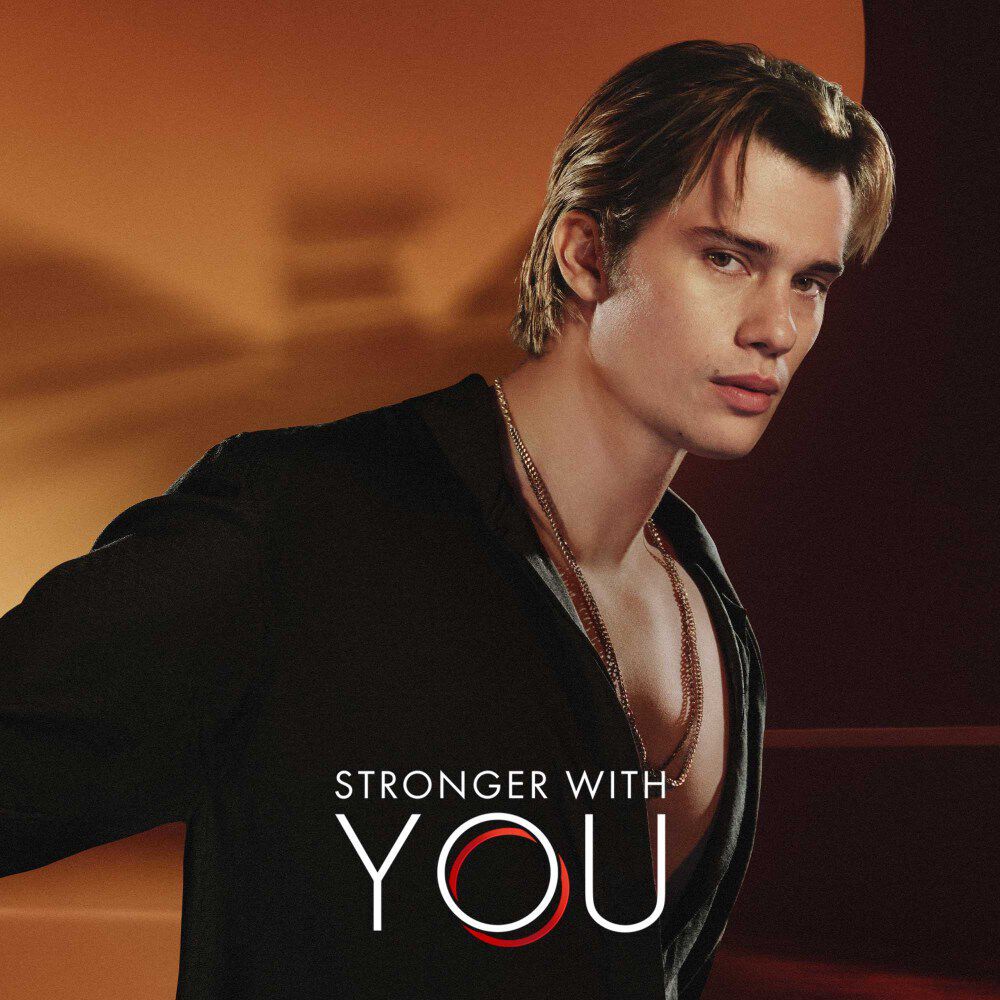 Nicholas Galitzine en het Stronger with You logo, met het wazige Emporio Armani logo achter hem.