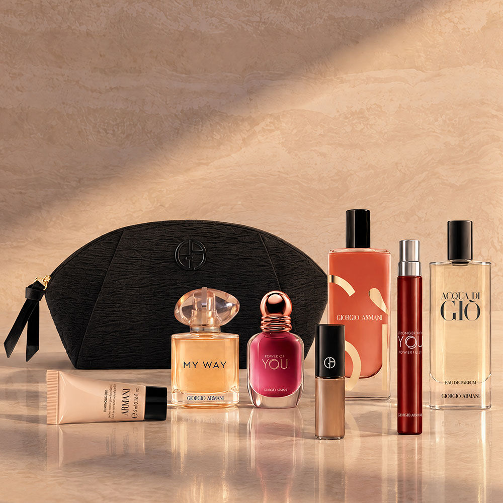 Een zwarte Armani Beauty-toilettas met parfums, make-up en huidverzorgingsproducten tegen een beige achtergrond.