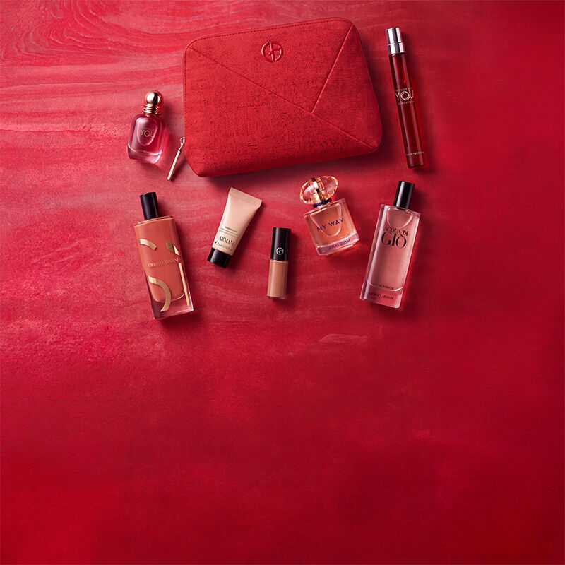 Drie Armani Beauty-producten — een lipproduct, de Power of You-geur en Luminous Silk foundation — tegen een rode achtergrond met textuur.