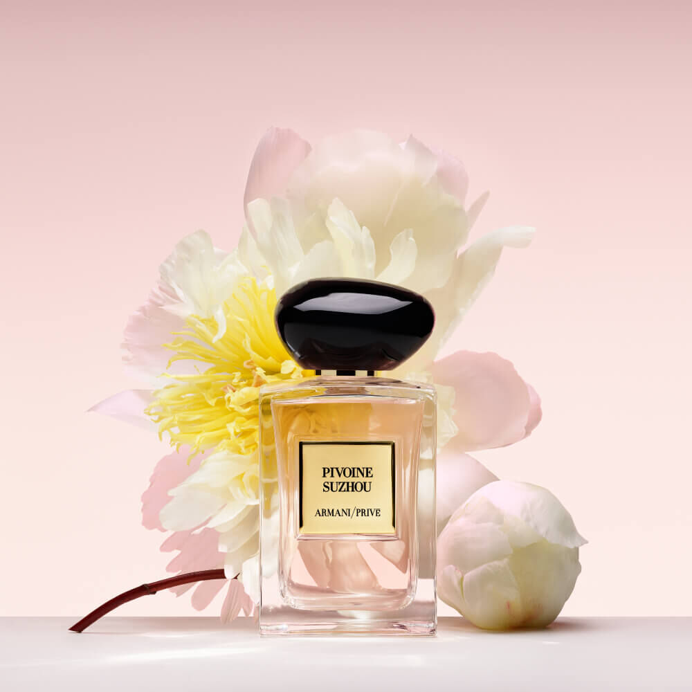 Armani Prive Les Eaux Pivoine Suzhou eau de parfum, transparent rectangular glass bottle with black rounded cap, surrounded by white peonies on a soft blush pink background