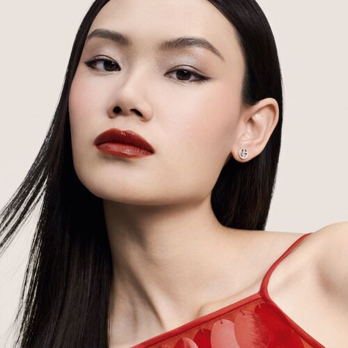 Een jonge vrouw met lang, stijl haar, rode lippen en een elegante outfit, poseert zelfverzekerd voor een lichte achtergrond.