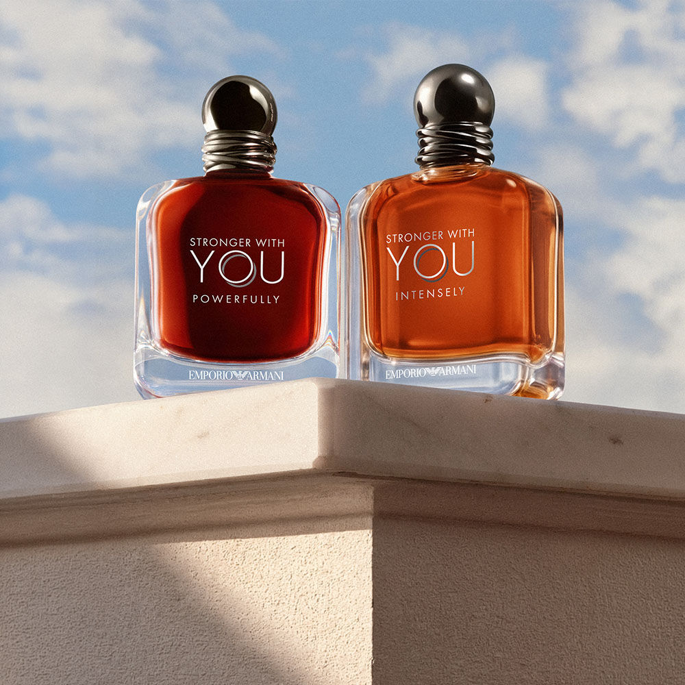 De geuren Stronger With You Powerfully en Stronger With You Intensely van Emporio Armani, gepresenteerd op een stenen sokkel tegen een blauwe lucht.​