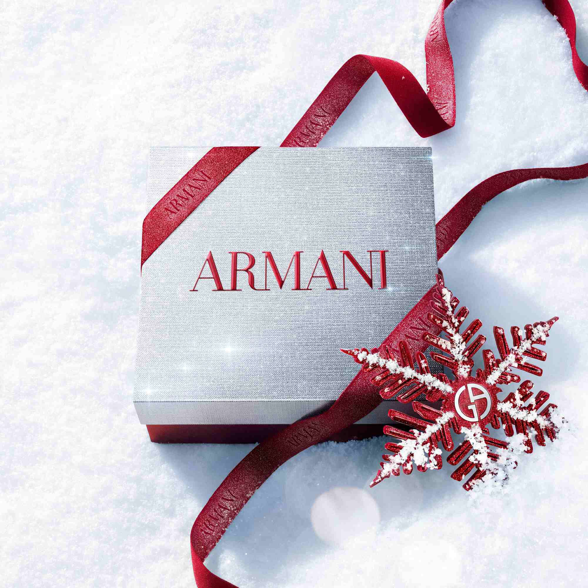 Ruby Power of You Eau de Parfum bottle with red Armani ribbon and jewelled snowflake on a snowy surface — Giorgio Armani women's fragrance, holiday gift set visual.