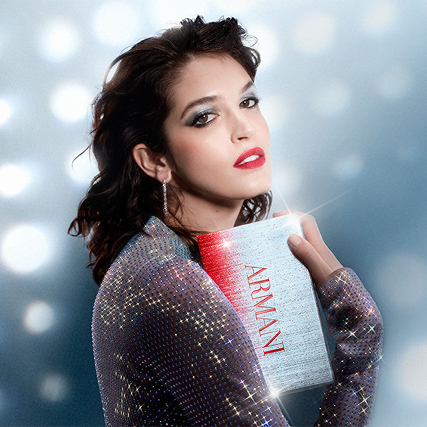Een mooie vrouw met een make-uplook voor Kerstmis houdt een geschenkdoos vast, tegen een achtergrond van dromerige lichtpunten in discostijl.