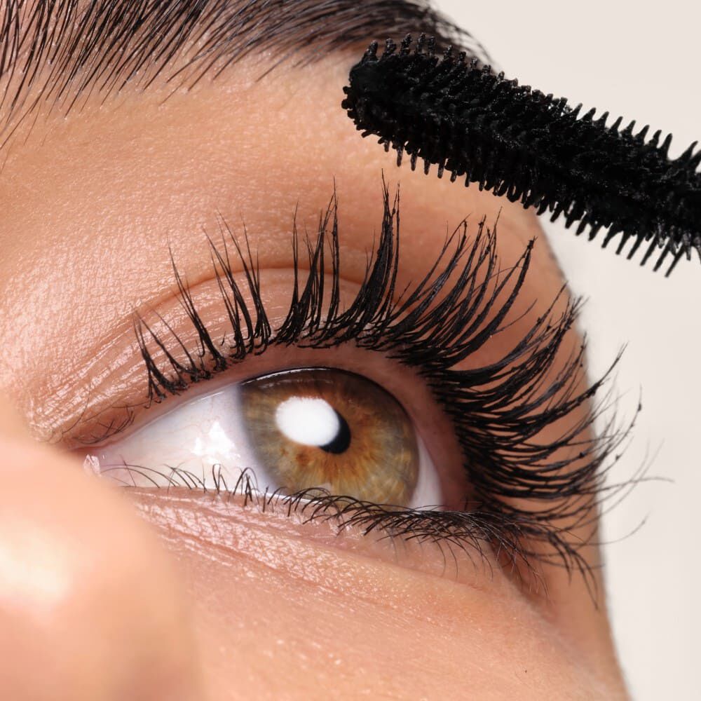 Een close-up van een oog met lange, volle wimpers die worden gemascareerd met zwarte mascara.