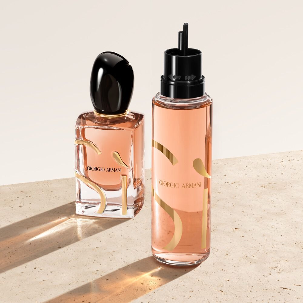 Twee flesjes Giorgio Armani Si Eau de Parfum staan op een beige ondergrond. Het flesje links is het klassieke Si parfumflesje, terwijl het rechterflesje een navulflesje is met een meer doorschijnende, perzikkleurige uitstraling.