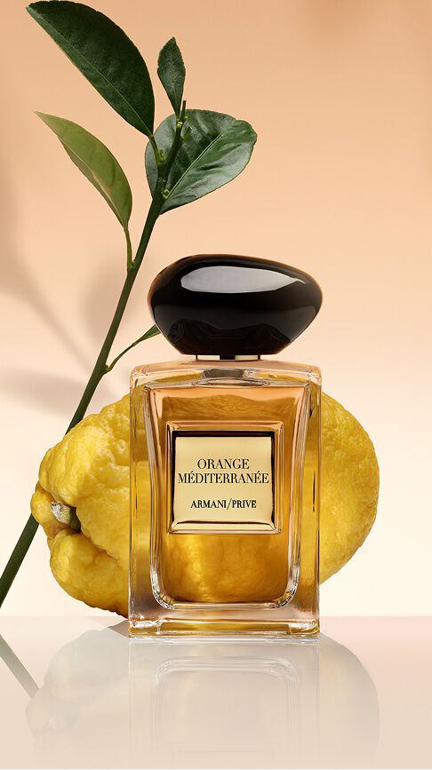 Armani/Prive Orange Mediterranee: een glazen flacon met goudkleurig parfum, voor een verse citrusvrucht en groene bladeren, die de zonovergoten warmte van de Middellandse Zee uitstraalt.