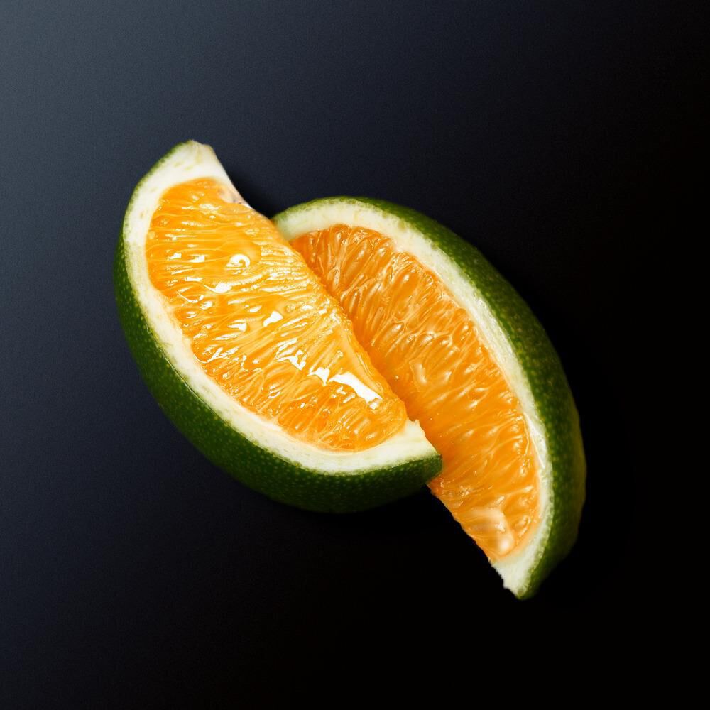 Een groene sinaasappel die doormidden is gesneden, met sappige oranje segmenten zichtbaar.