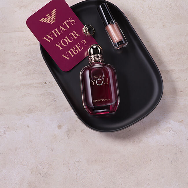 Flacon van de Power of You-geur van Emporio Armani en een metallic lipproduct op een zwart dienblad, naast een kaart met de tekst ‘What’s Your Vibe?’.