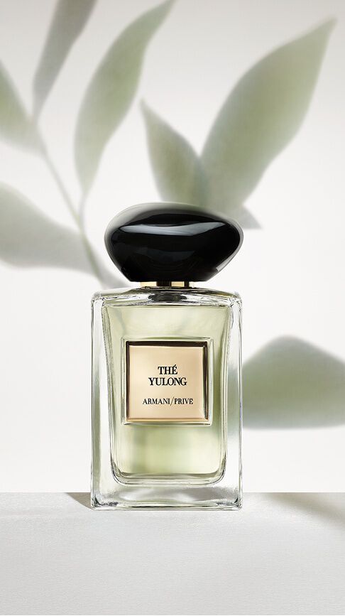 Armani/Prive The Yulong: een heldere flacon met een lichtgroene essence, geplaatst tegen een minimalistische achtergrond van zachte bladschaduwen, die de serene balans van thee belichaamt.