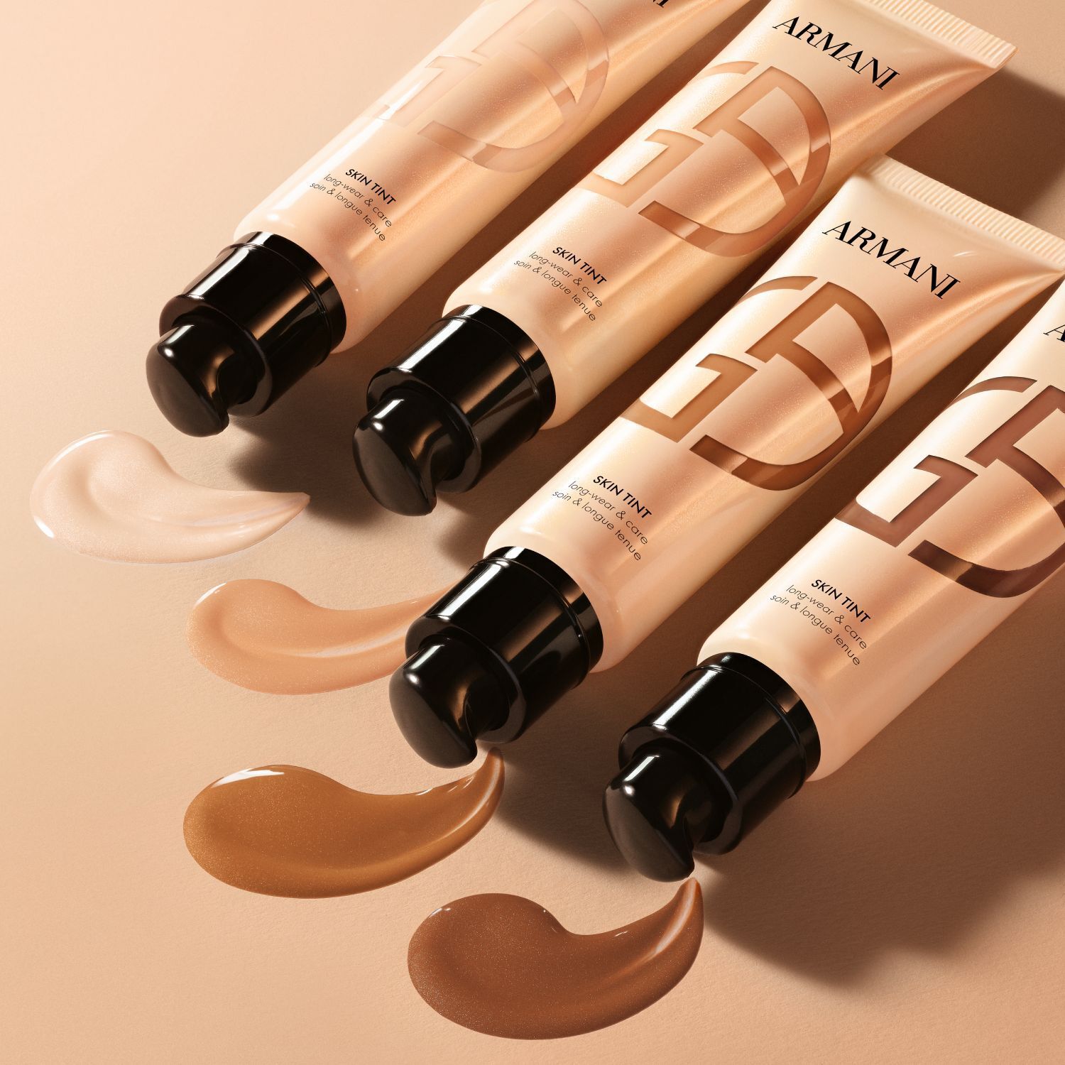 Vier Armani Skin Tint tubes met uitgesmeerde swatches die een reeks tinten tonen.