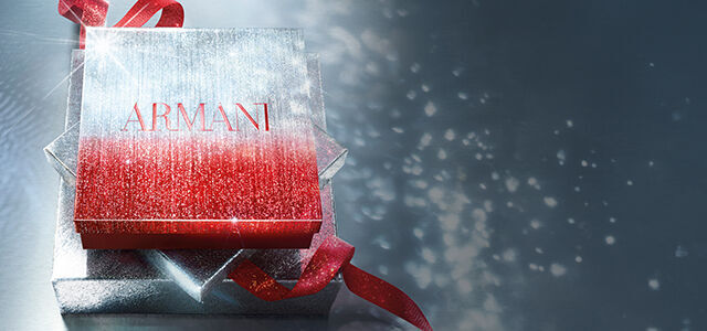 Armani geschenkdoos in sprankelend rood en zilver met een rood lint, tegen een glinsterende achtergrond.