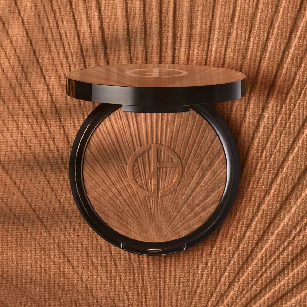 A bronzing powder compact with a sleek, black casing and a textured interior background, featuring a sunburst design.