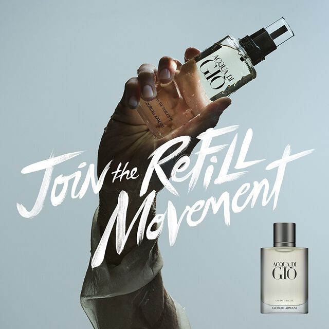 Een krachtig beeld: een hand houdt de Acqua di Gio navulling voor de lucht, met de tekst "Join the Refill Movement" in penseelstreken. Symbool van duurzame luxe en de tijdloze mariene frisheid van het Huis Armani.