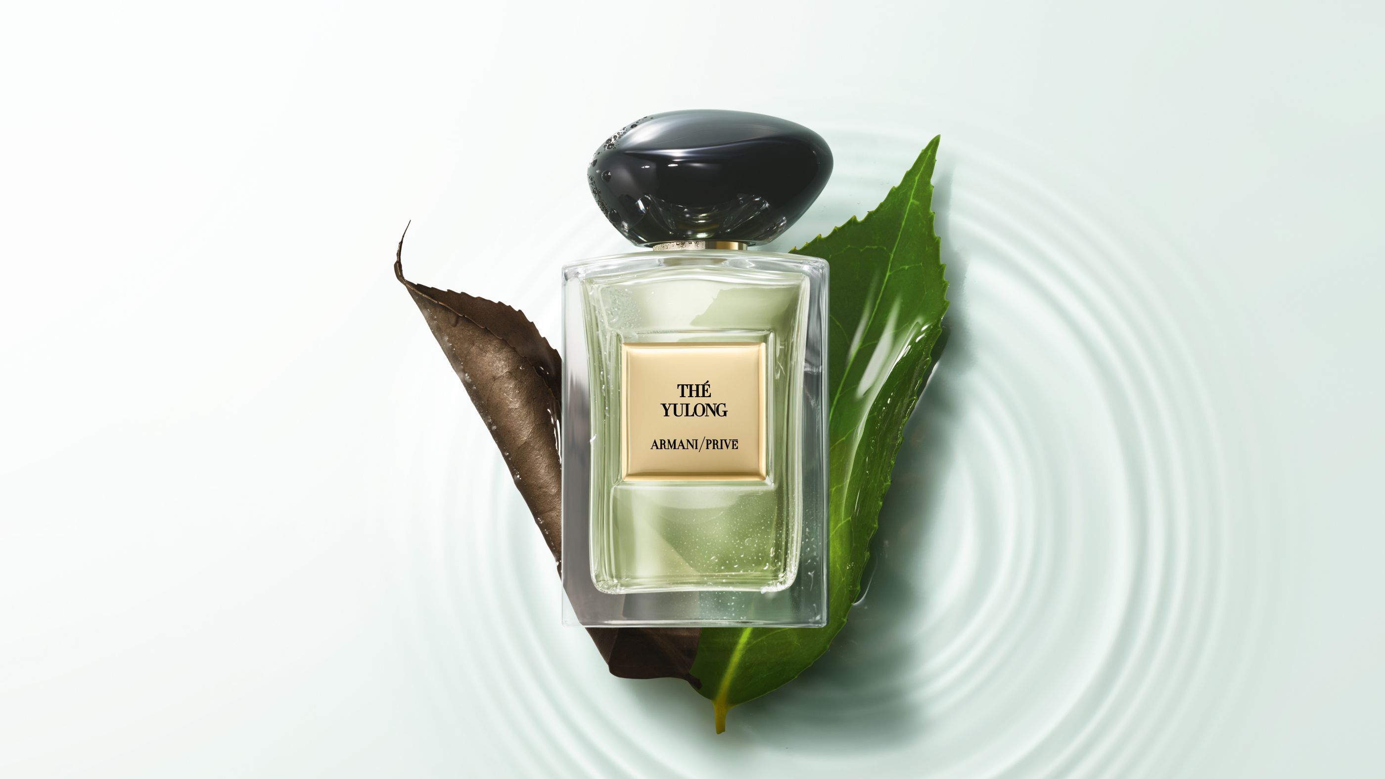 Armani/Prive "The Yulong" parfumflesje rustend op bladeren boven rimpelend water.