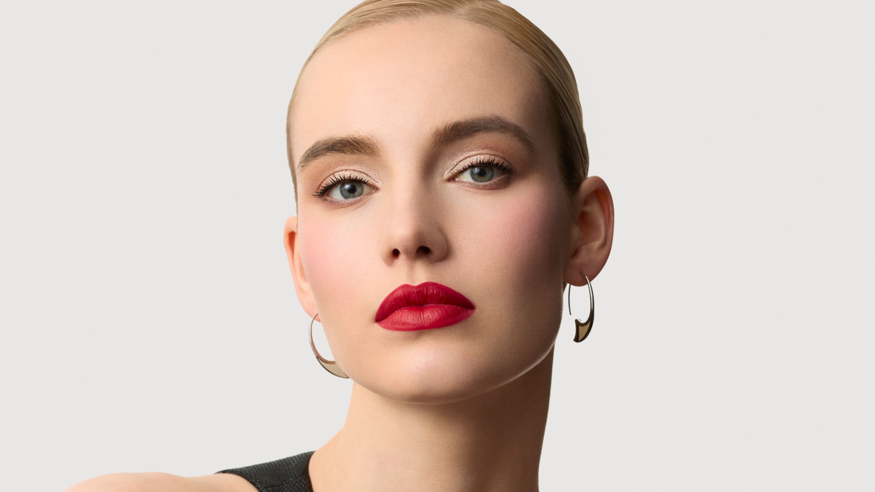 Close-up van een blonde vrouw met elegante make-up en felle rode lippenstift.