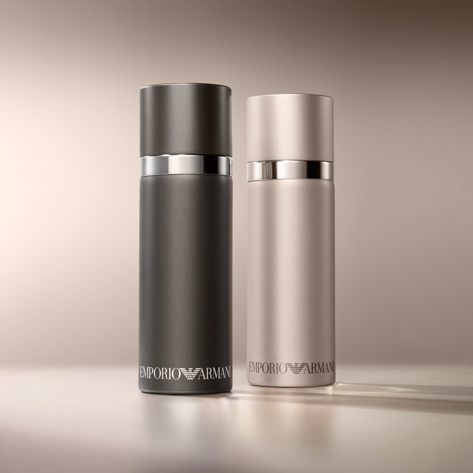 Een verfijnd duo van Emporio Armani parfumflessen: een matzwarte "He"-fles gecombineerd met een lichtere, mogelijk rosegouden of zilveren "She"-fles, op een zachte, warmgekleurde achtergrond.