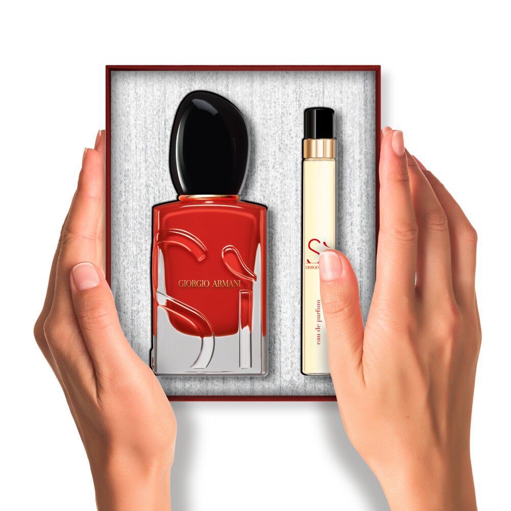 Handen die een Armani Si Passione-parfum en reisspray vasthouden die in een geschenkdoos worden geplaatst.