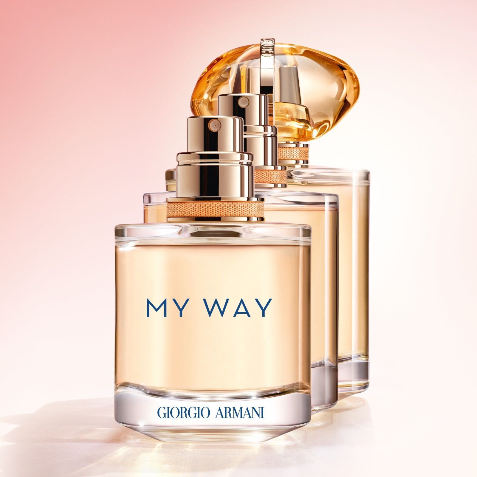Armani My Way Sunny Vanille parfumflesje wordt getoond in drie verschillende maten met zijn elegante gouden dop, wat luxe en verfijning weerspiegelt op een pastelachtergrond.