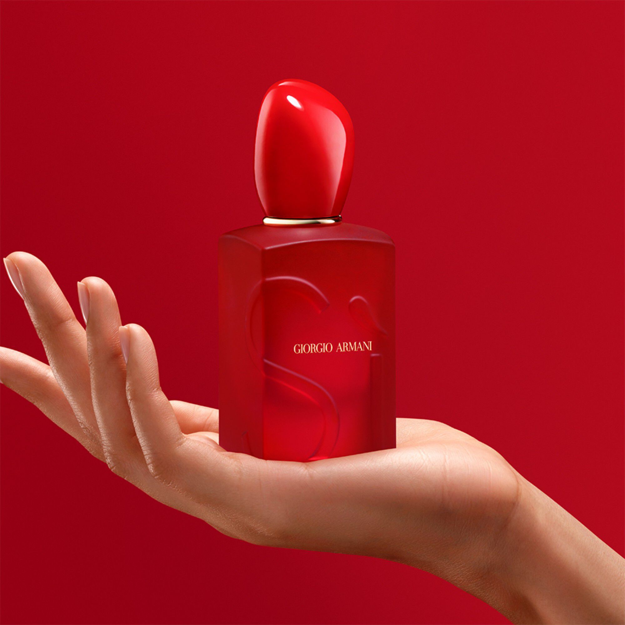 Hand die de Giorgio Armani Si Passione Red Bloom fles vasthoudt op een rode achtergrond.