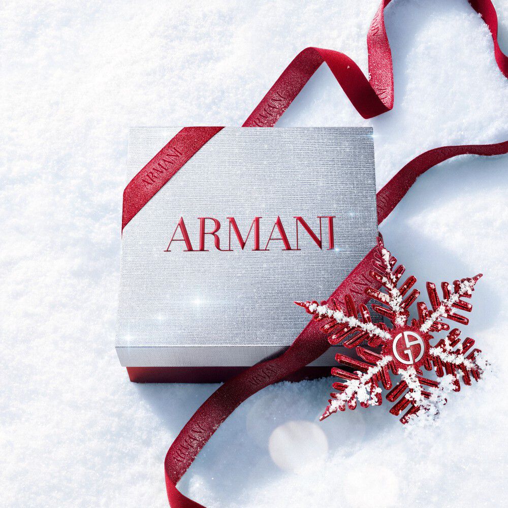 Armani beauty Holiday 2026 white gift box tied with a red ribbon and snowflake decoration, photographed on a snowy surface, 1x1 digital still.