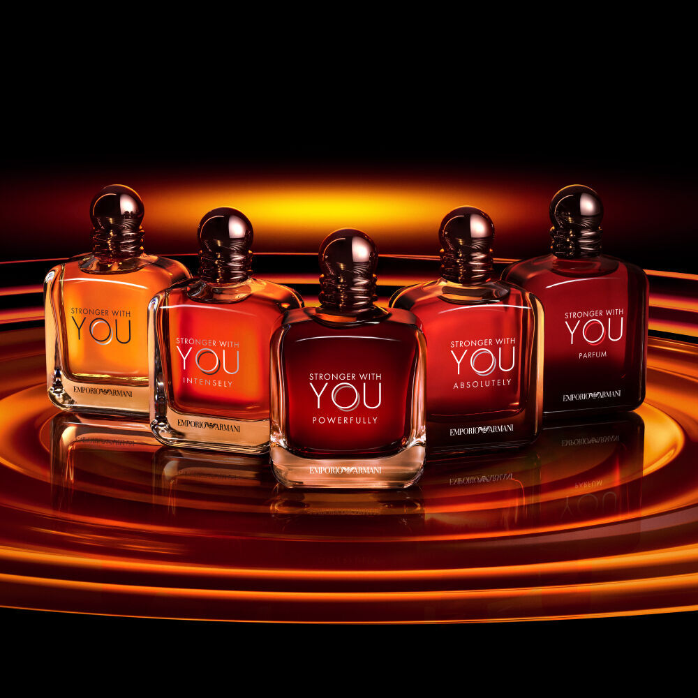 Vijf Armani Stronger With You parfumflessen, elke variant stralend op een stralende, amberkleurige achtergrond, waarmee de volledige collectie de gedurfde elegantie van de collectie laat zien.