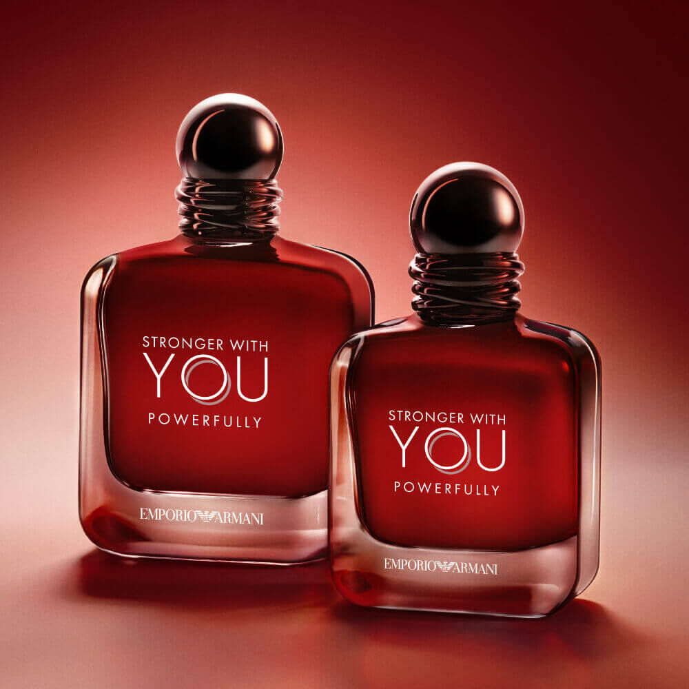 Twee Armani Stronger With You Krachtig 50 ml en 100 ml flessen naast elkaar, gloeiend op een rode achtergrond.