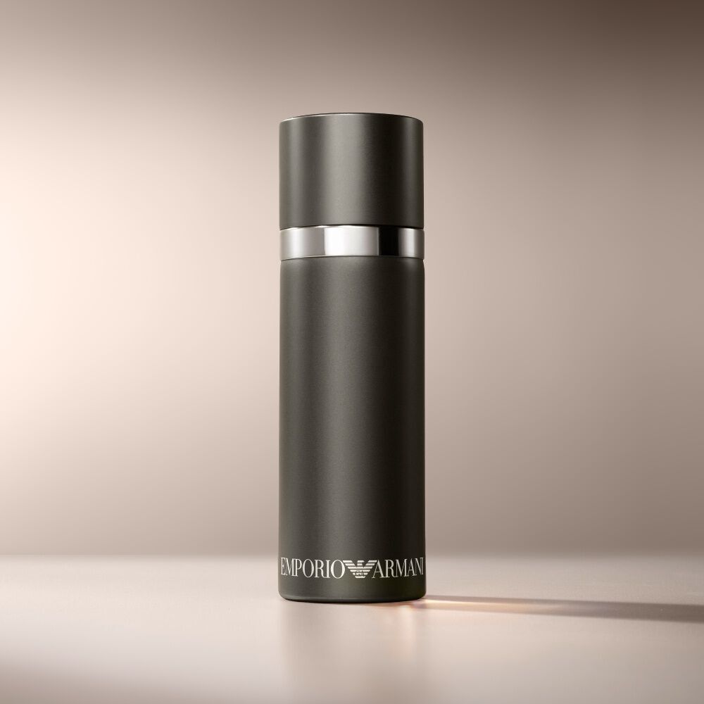 Een matzwarte cilindervormige Emporio Armani "He" parfumfles is elegant geplaatst op een warme, lichtbruine achtergrond.