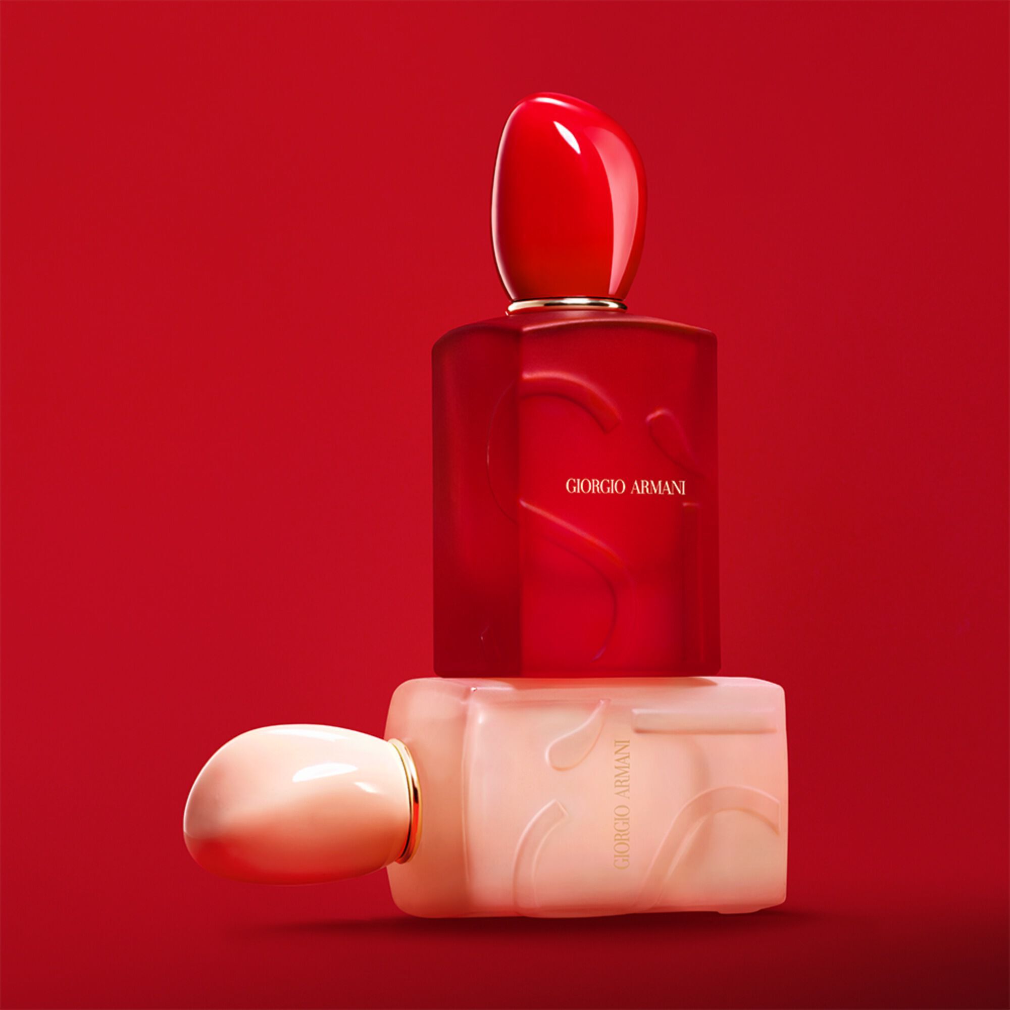 Giorgio Armani Si Nude Bloom en Si Passione Red Bloom flessen opgestapeld op een rode achtergrond.