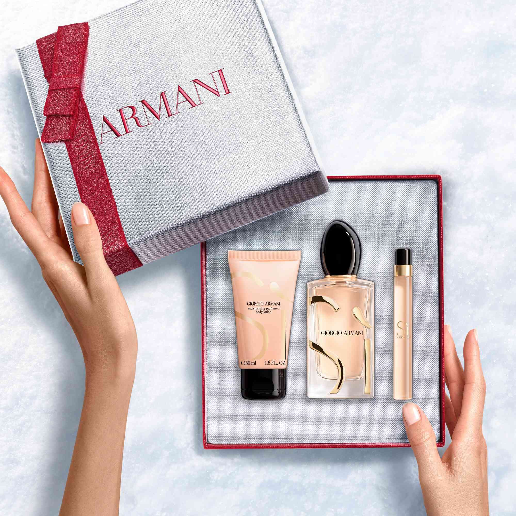 Hands onthullen een roodlint witte Armani cadeaubox met Si Eau de Parfum 100 ml, reismaat 10 ml en 50 ml geparfumeerde bodylotion — een verfijnde bloemenparfum voor dames.