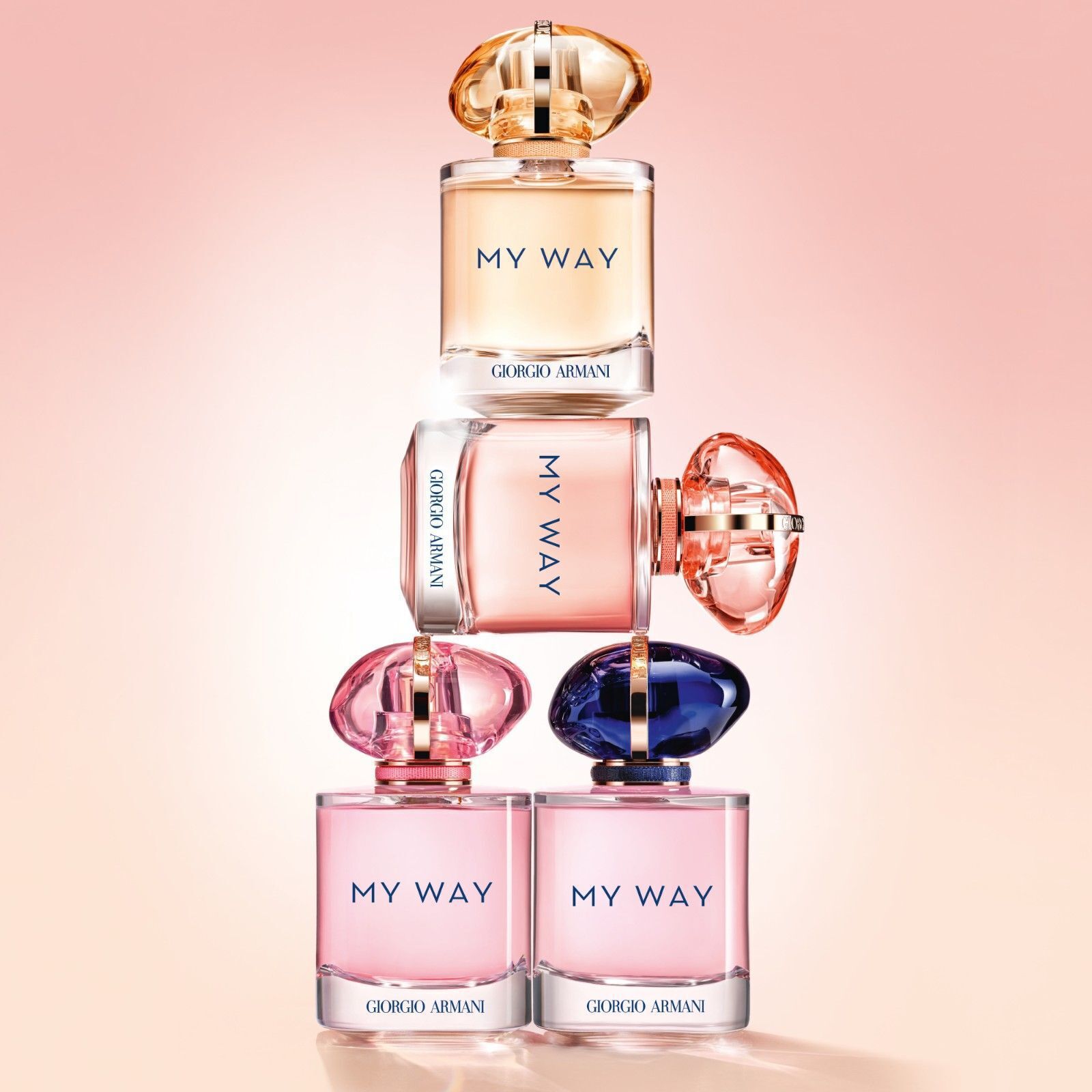 Stapel van vier Armani My Way parfumflessen in verschillende tinten en maten, die de variatie en speelse stijl van de collectie illustreren.