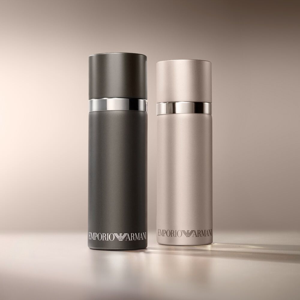 Een verfijnd duo van Emporio Armani parfumflessen: een matzwarte "He"-fles gecombineerd met een lichtere, mogelijk rosegouden of zilveren "She"-fles, op een zachte, warmgekleurde achtergrond.