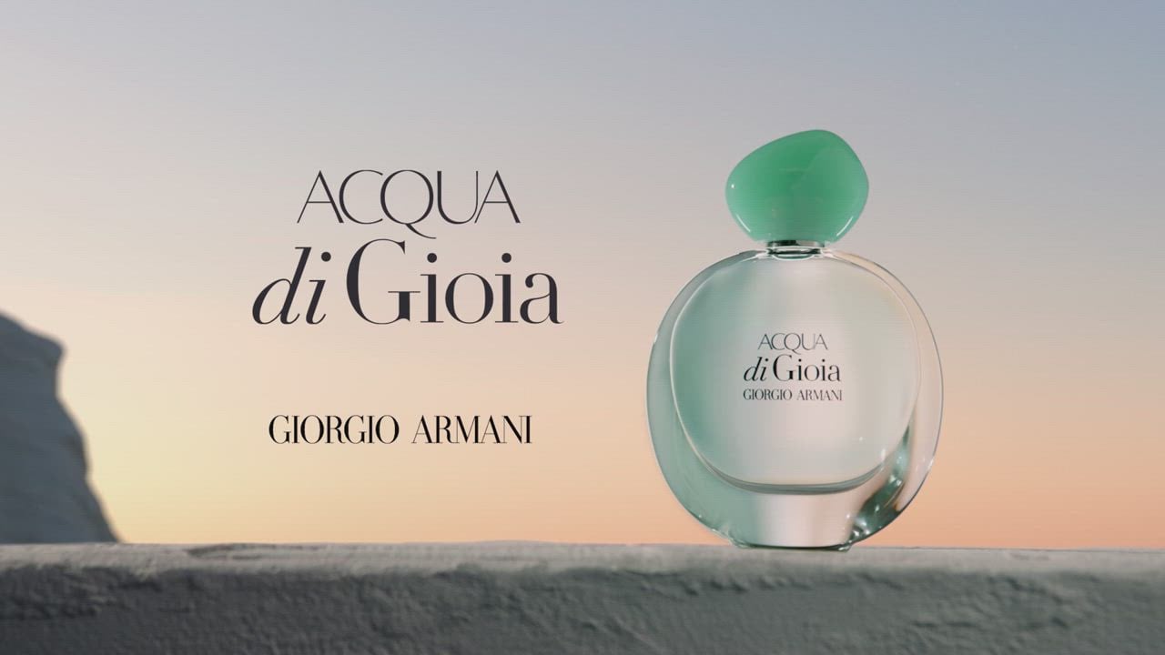Een fles Acqua di Gioia parfum van Giorgio Armani, met een groene dop, voor een zachte achtergrond bij zonsondergang.